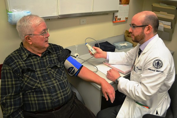 Dr. Rene Cuadra, a resident who assists in the INFINITY trial, shows study participant Gerald Kehoe how to use a 24-hour blood pressure monitor. (Chris DeFrancesco/UConn Health Photo)